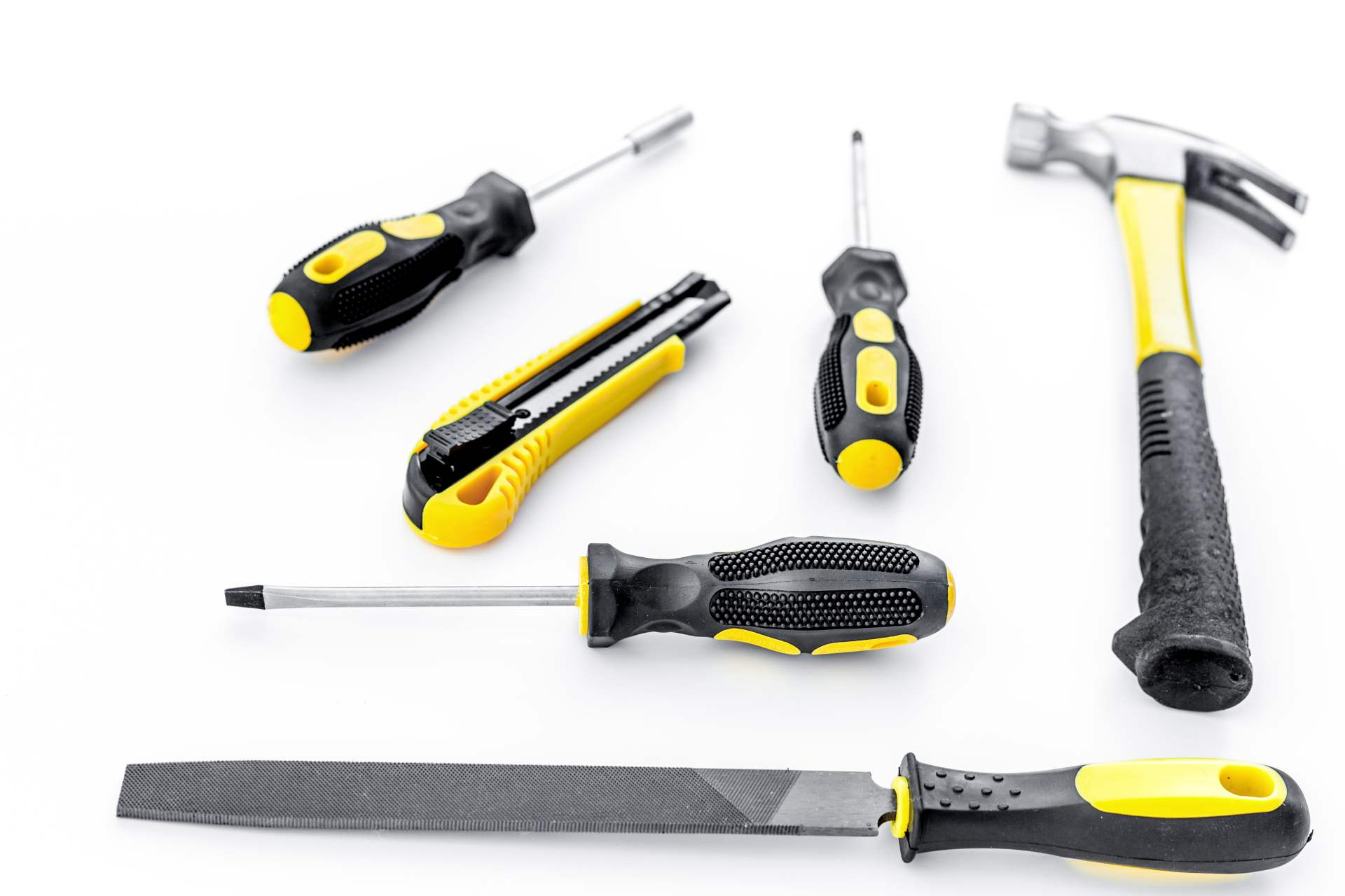 Yellow and black hand tools on a white surface, including screwdrivers, a hammer, and a utility knife.