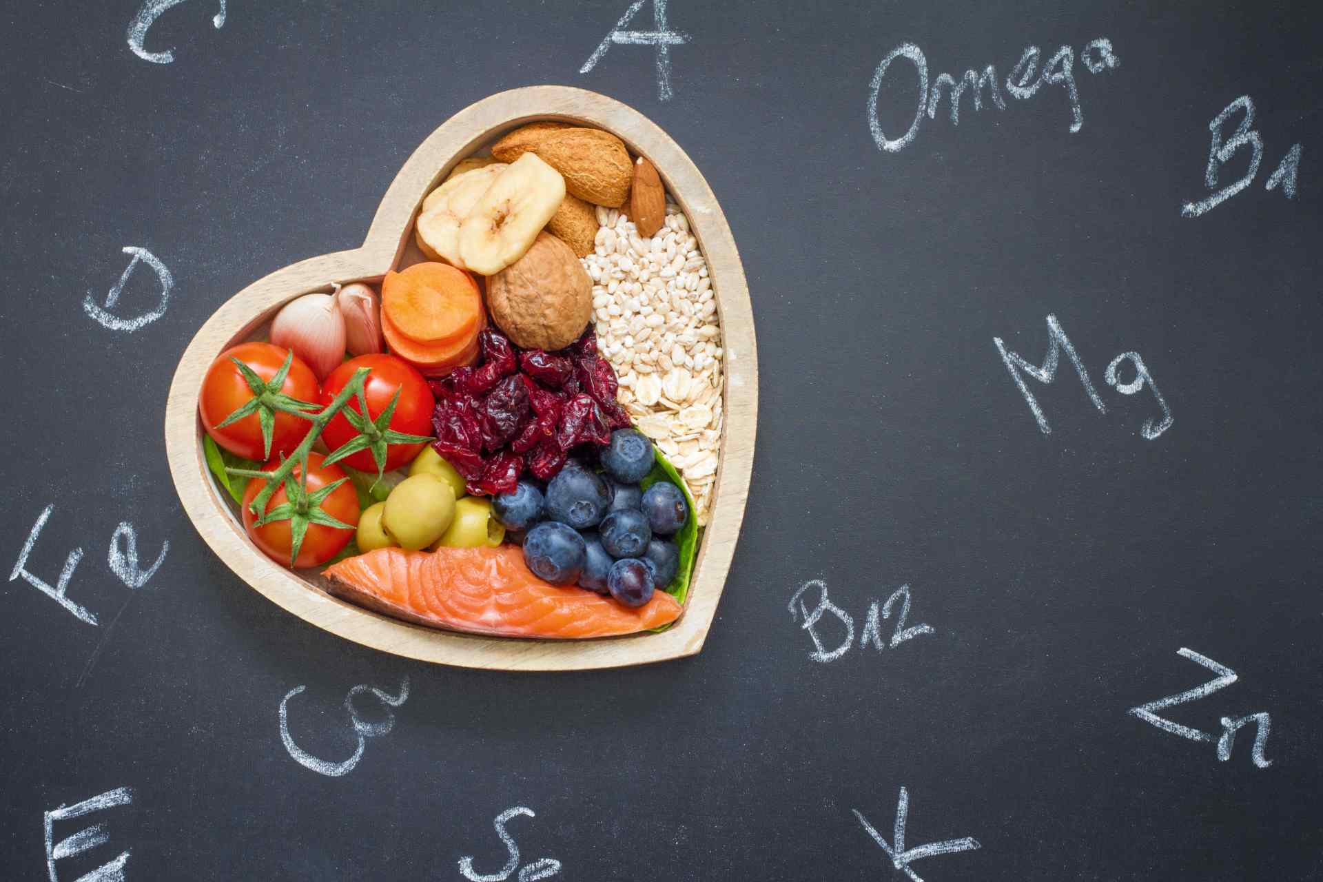 Heart-shaped bowl of healthy foods on a chalkboard with nutrition labels.