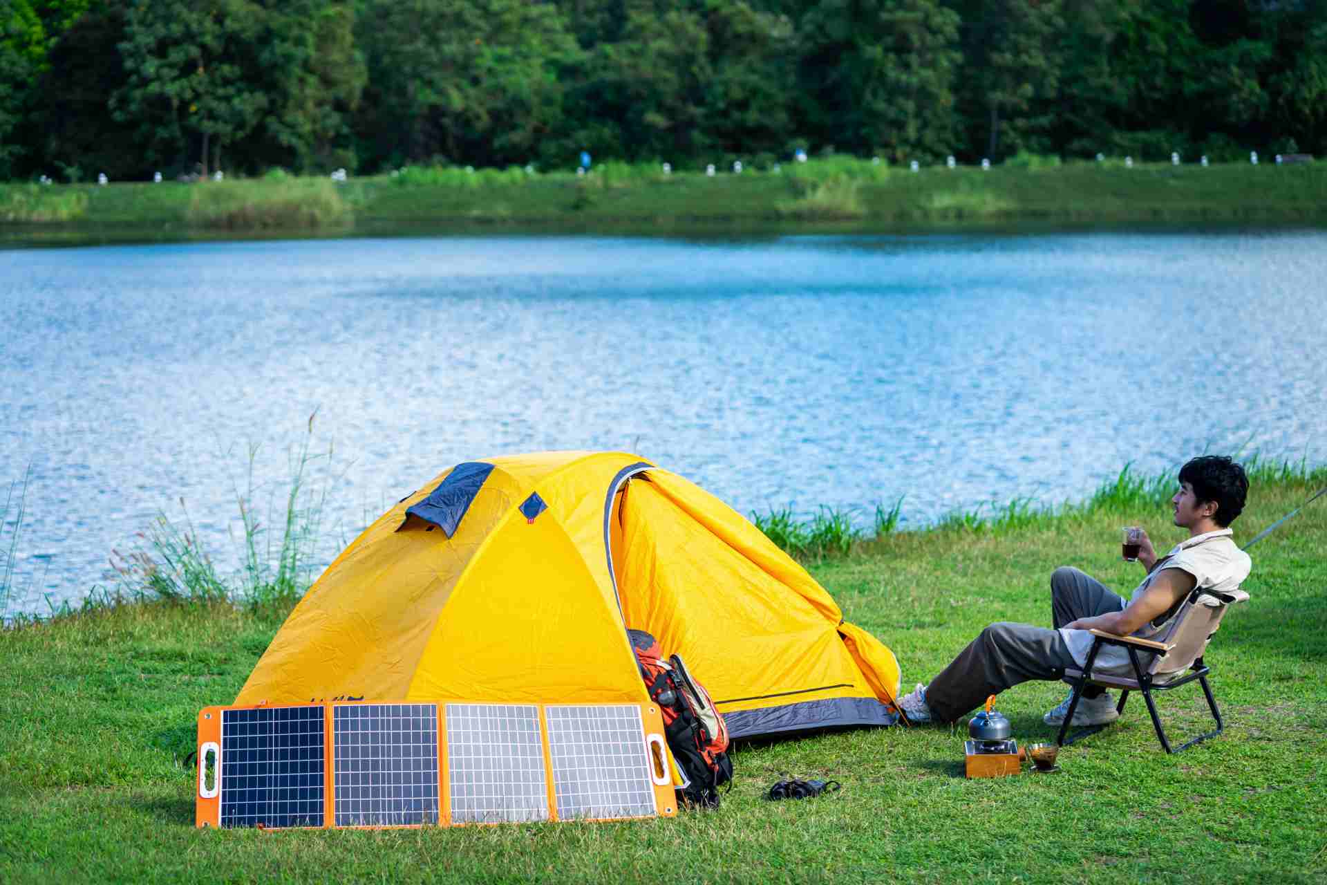 A bright yellow tent by a lake with solar panels set up in front, showcasing solar power for camping in serene natural environments.