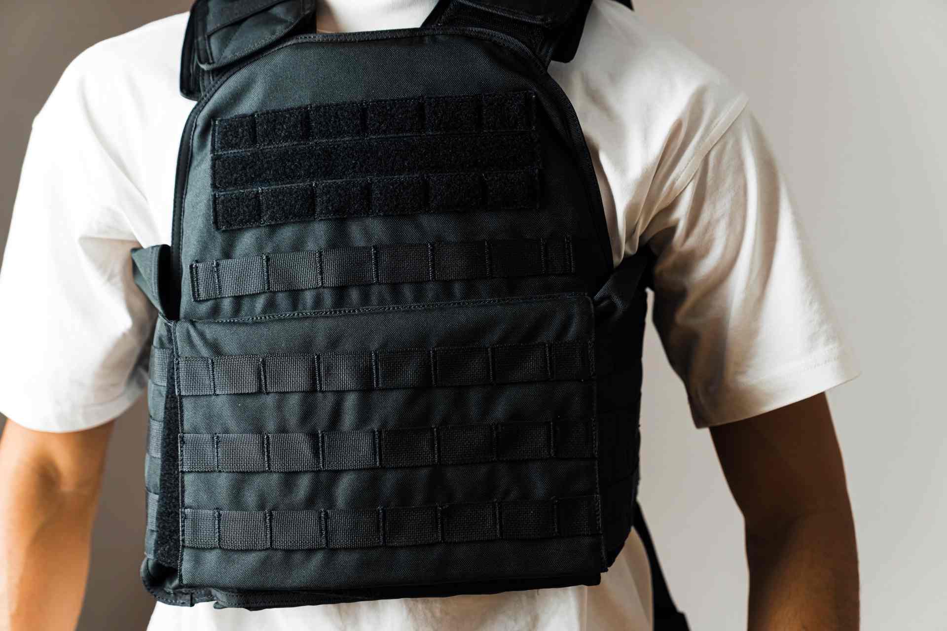 A person wearing a black tactical plate carrier over a white shirt, showcasing front MOLLE webbing and lightweight design for adaptability.