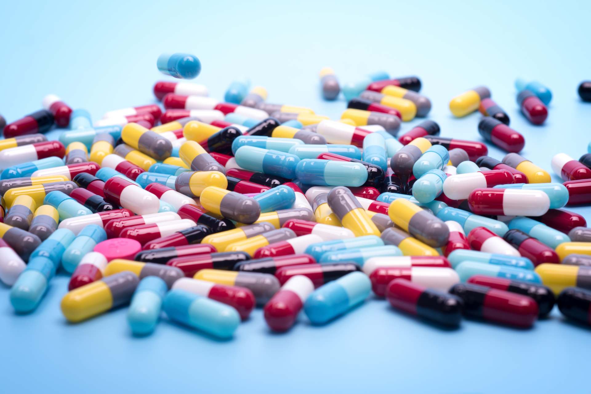 A pile of colorful antibiotic capsules on a blue surface.