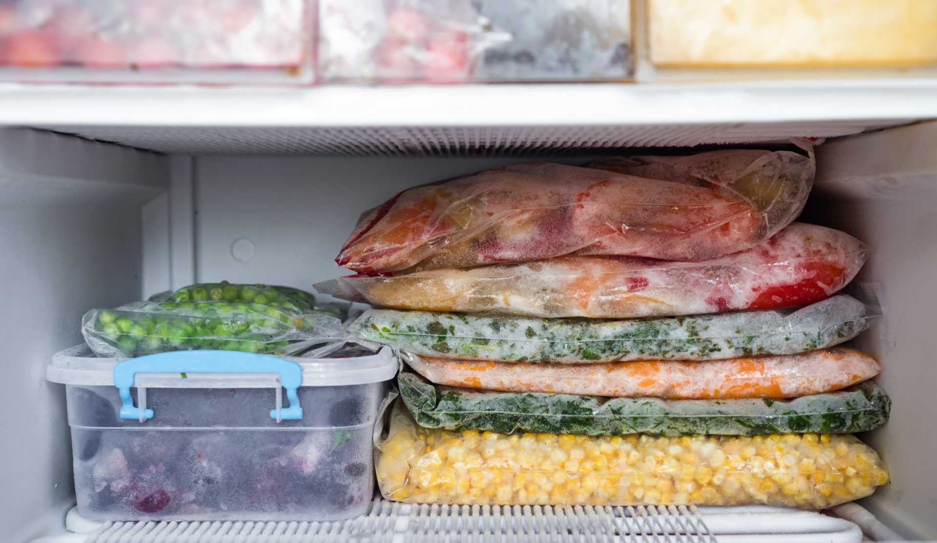Frozen vegetables like corn, peas, and mixed produce stored in sealed plastic bags inside a freezer.