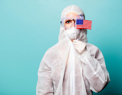 A person in full protective medical gear holding a small American flag, symbolizing the healthcare response during the COVID-19 pandemic in the United States.