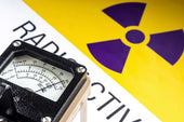 A close-up of a radiation measurement device in front of a large radioactive warning sign. The device shows detailed measurements in microsieverts per hour, illustrating the need for precision in radiation detection.