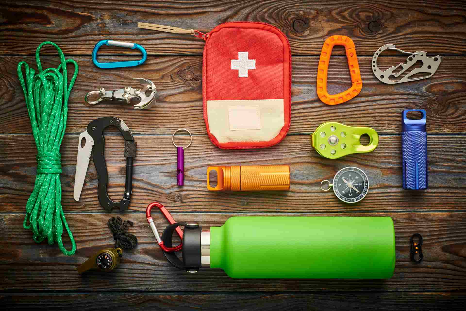  Survival tools like a first aid kit, rope, flashlight, and water bottle on a wooden surface.
