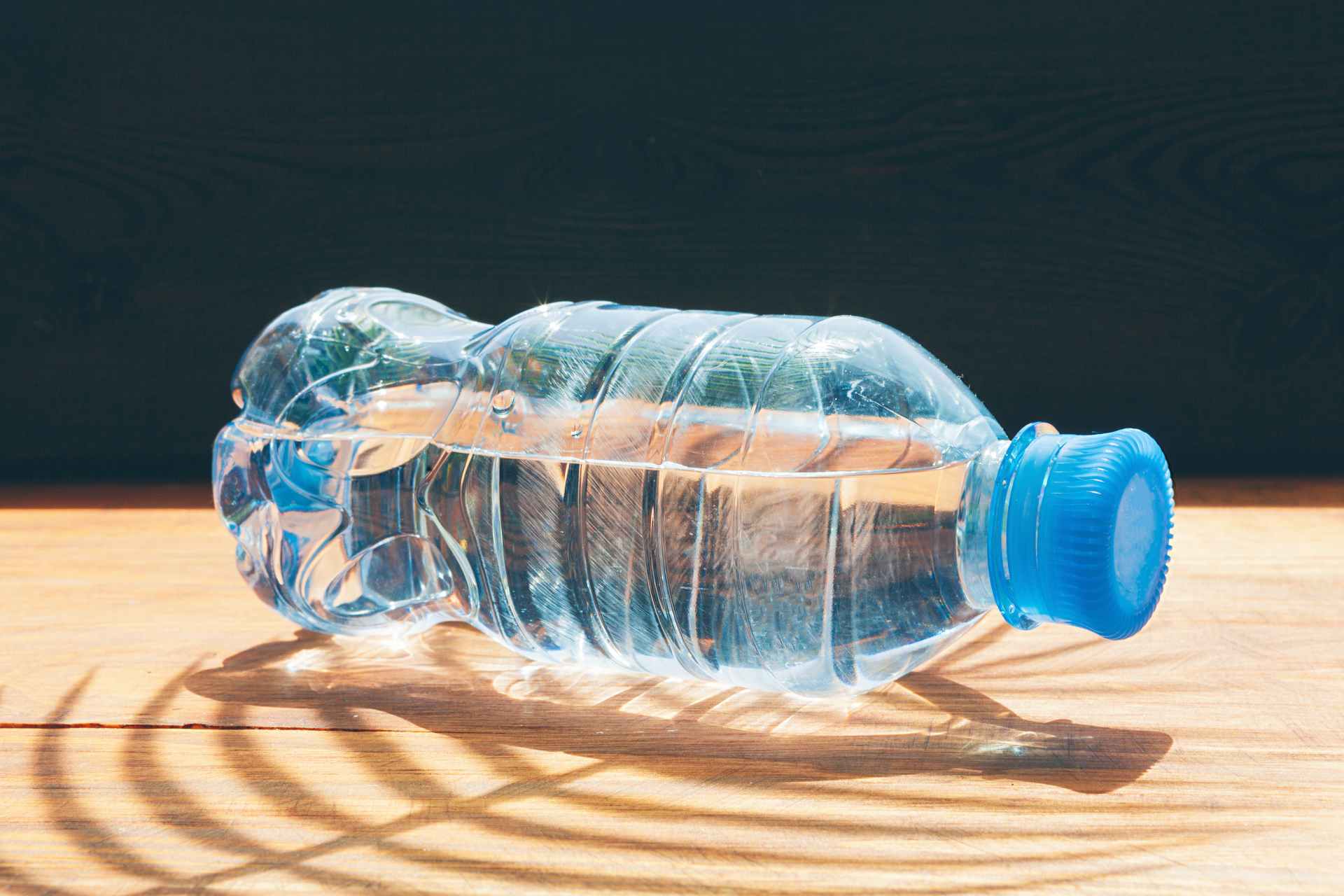 A clear plastic water bottle on a wooden surface with sunlight shadows, showing bottled water's portability.