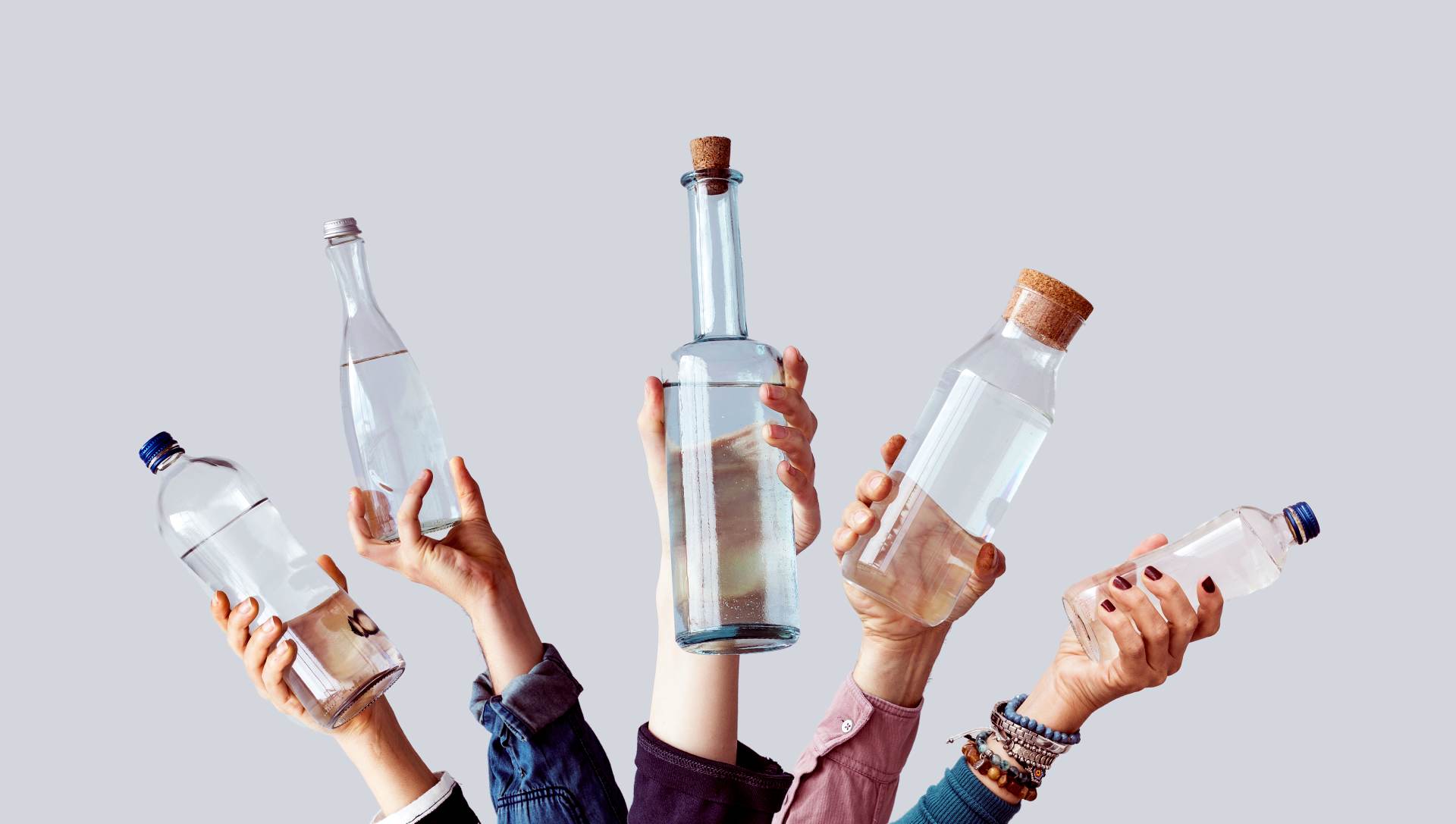 Hands holding various bottles of clear homemade alcohol.