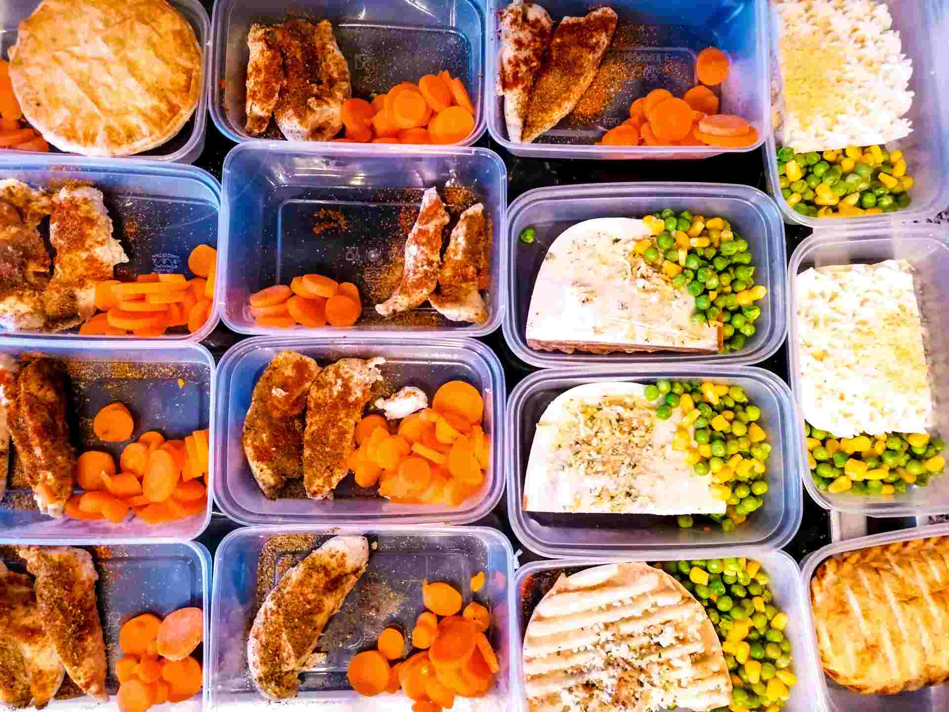 Neatly arranged freezer meal containers with chicken, carrots, peas, rice, and wraps, ready for storage.